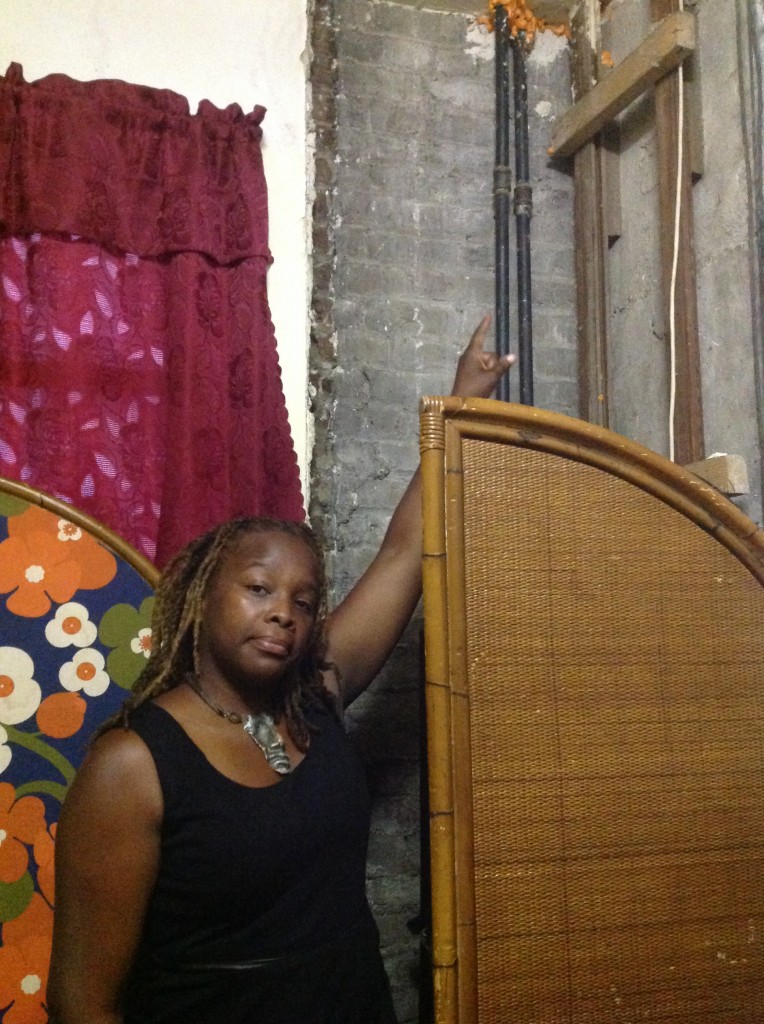 TENANT SHANEQUA CHARLES stands by a neighbor’s exposed wall where an old-fashioned dumbwaiter once stood. Photo by Kasia Romanowska